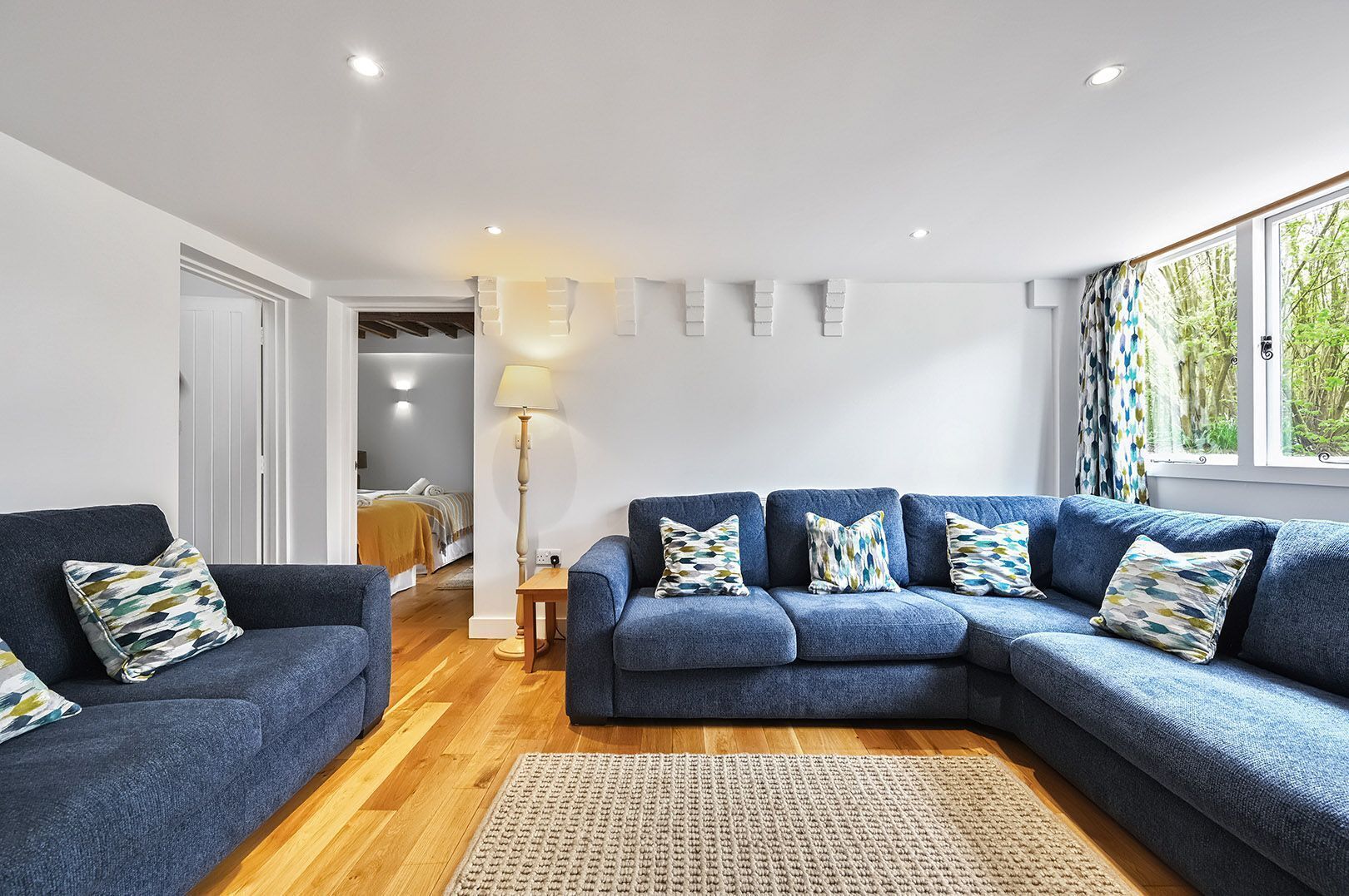 Un salon moderne avec un canapé bleu, un plancher en bois et une vue sur la verdure par la fenêtre.