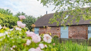 A brick building with a sloped roof, a chimney, and a small garden area with pink flowers and green grass.