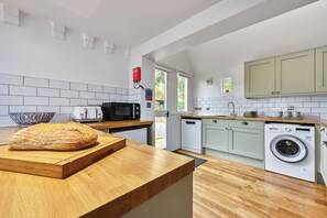 A modern kitchen with a wooden countertop, a loaf of bread, a microwave, a toaster, and a washing machine. - Great Higham Oast and Cottages by Bloom Stays -  sleeps 18 guests  in 6 bedrooms (Sittingbourne)