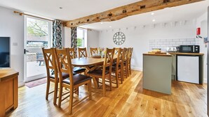 A dining area with wooden chairs and a table, a kitchen with a microwave and refrigerator, and a large window with curtains.