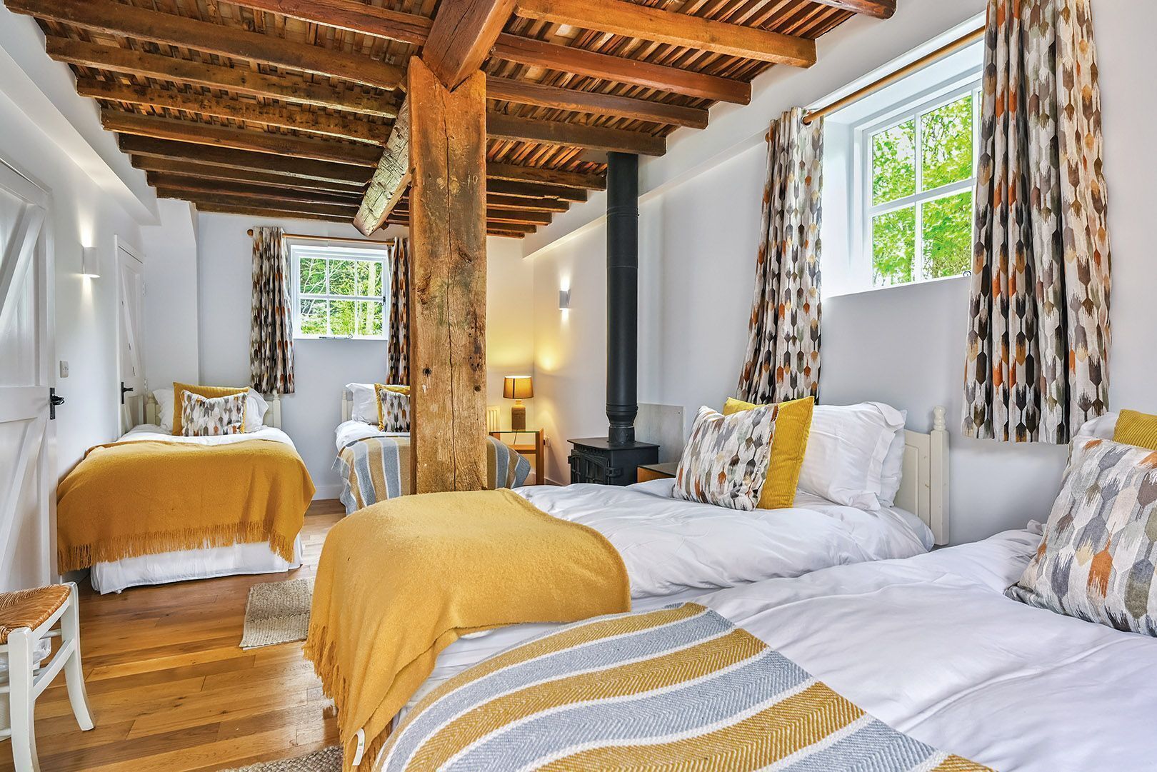 A room with two beds, a wooden ceiling, a fireplace, and a window with curtains.