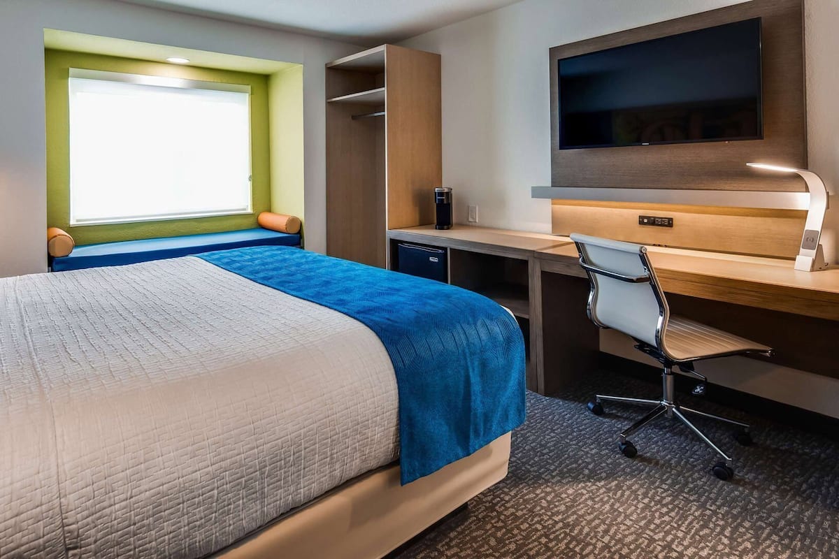 Una habitación de hotel con cama, escritorio, silla, televisor y ventana con vistas.