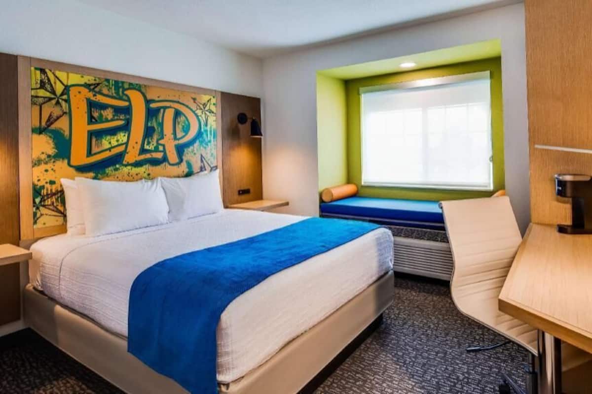Habitación de hotel con cama, escritorio, ventana con vistas, un cuadro de colores en la pared y una pared de acento verde.