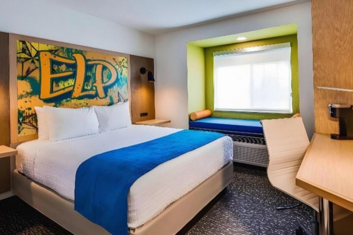 Habitación de hotel con cama, escritorio, ventana con vistas y un cuadro llamativo en la pared.