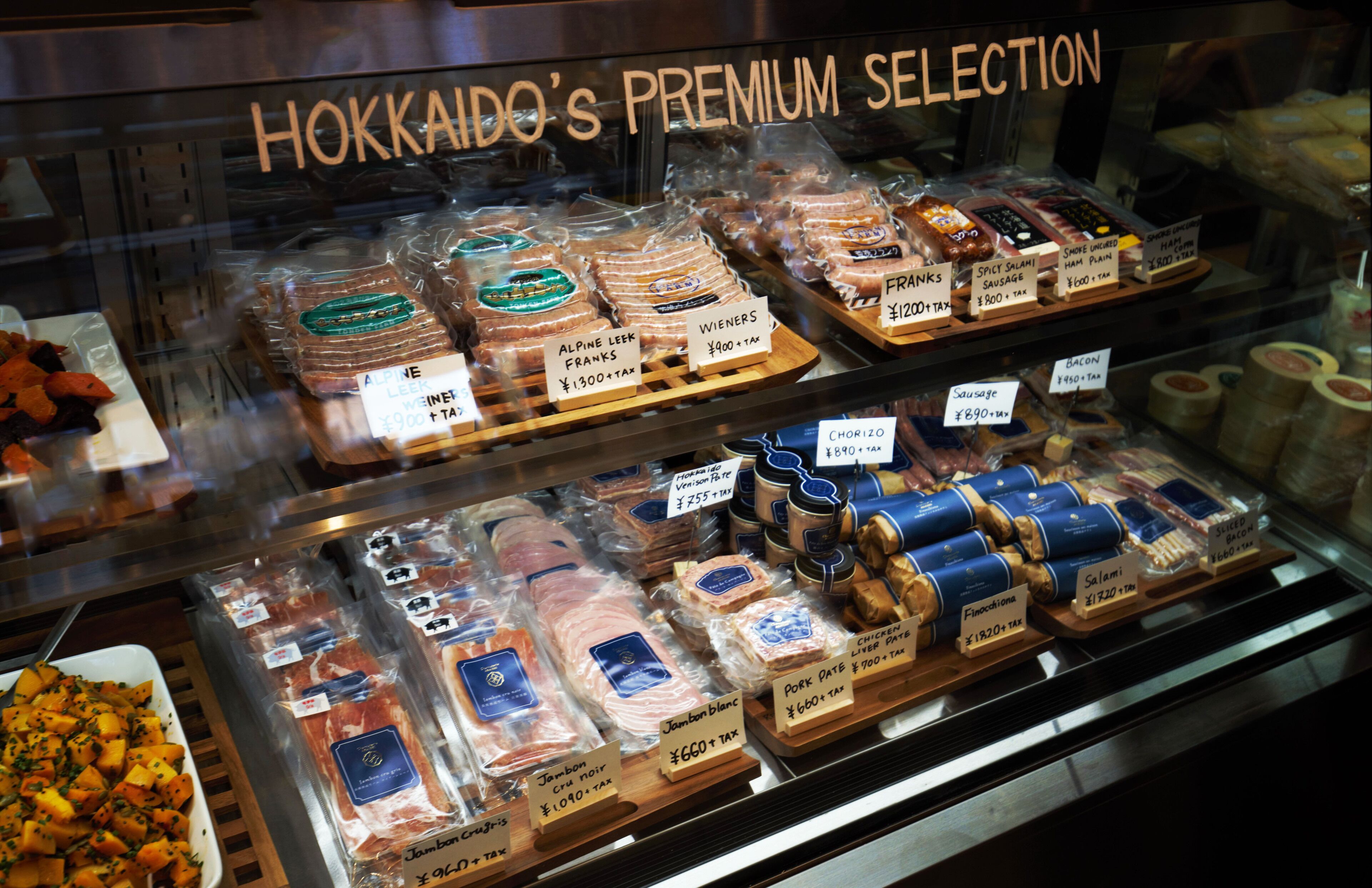 Un présentoir de charcuterie proposant divers types de viandes et de fromages emballés, chacun étant muni d’une étiquette indiquant son prix.