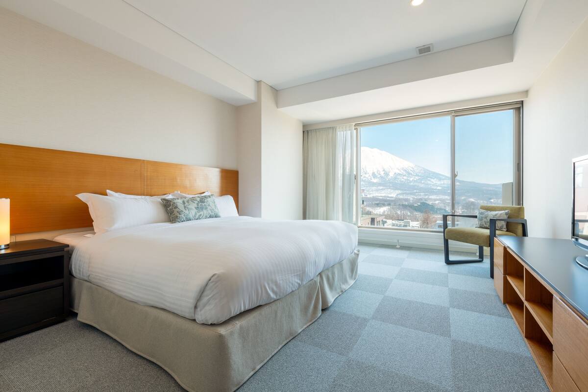 Una habitación de hotel moderna con una cama grande, un escritorio y vistas a la montaña.