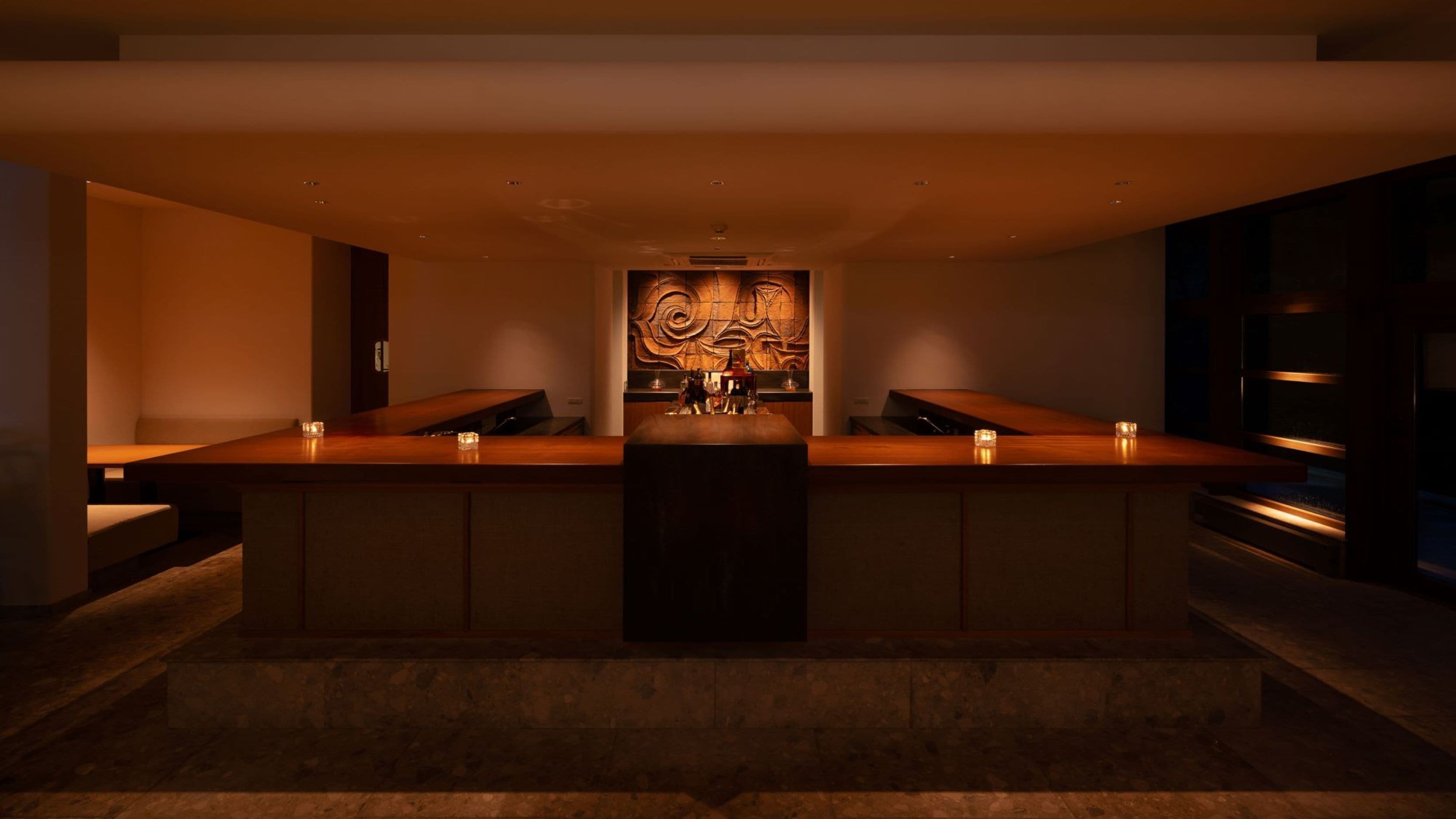 Eine moderne Bar mit einer langen Theke, zwei Sitzbereichen und einer Wand mit abstrakter Kunst.