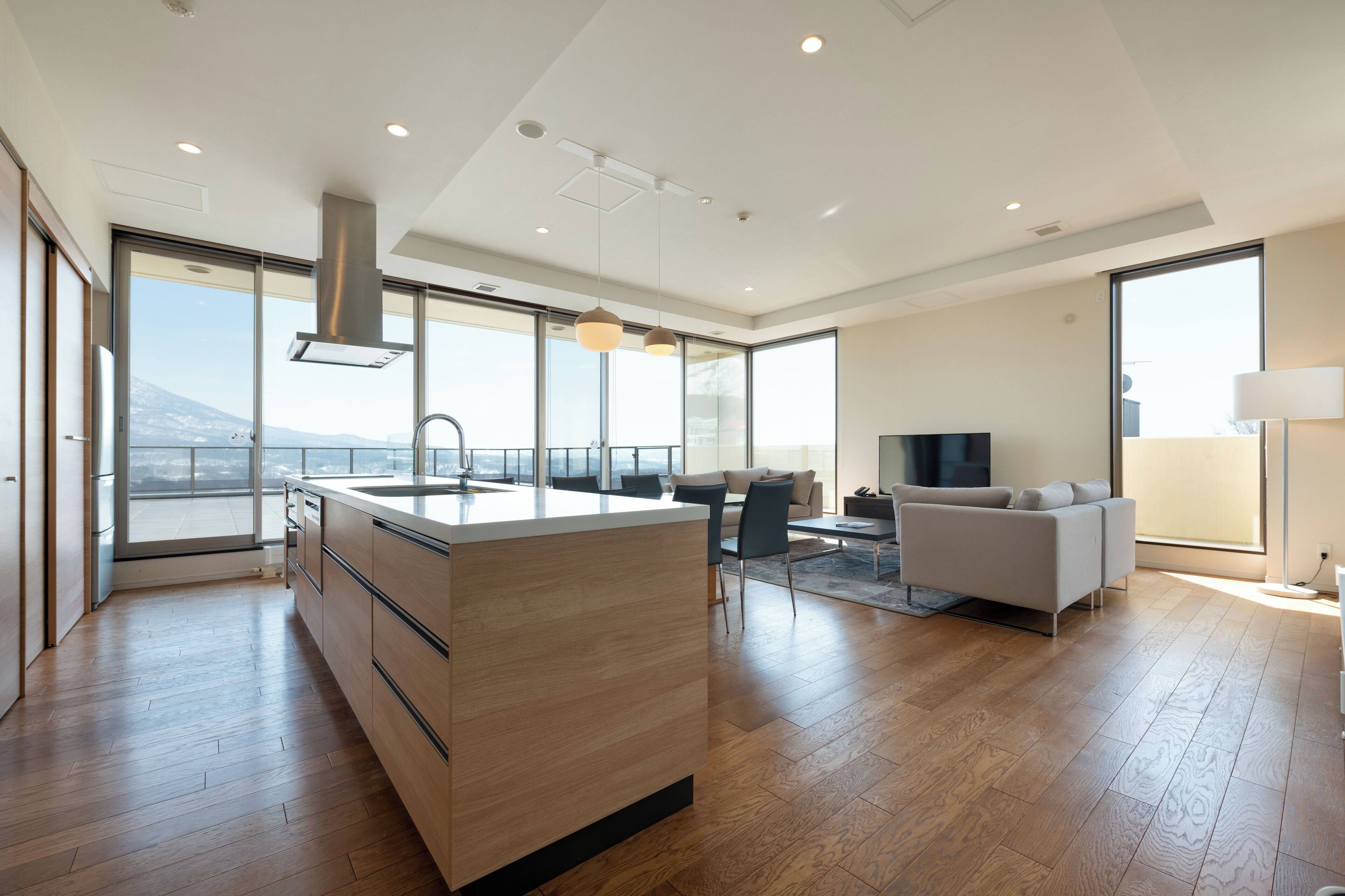 Een moderne keuken met een groot eiland, houten vloeren en grote ramen met uitzicht op de stad.