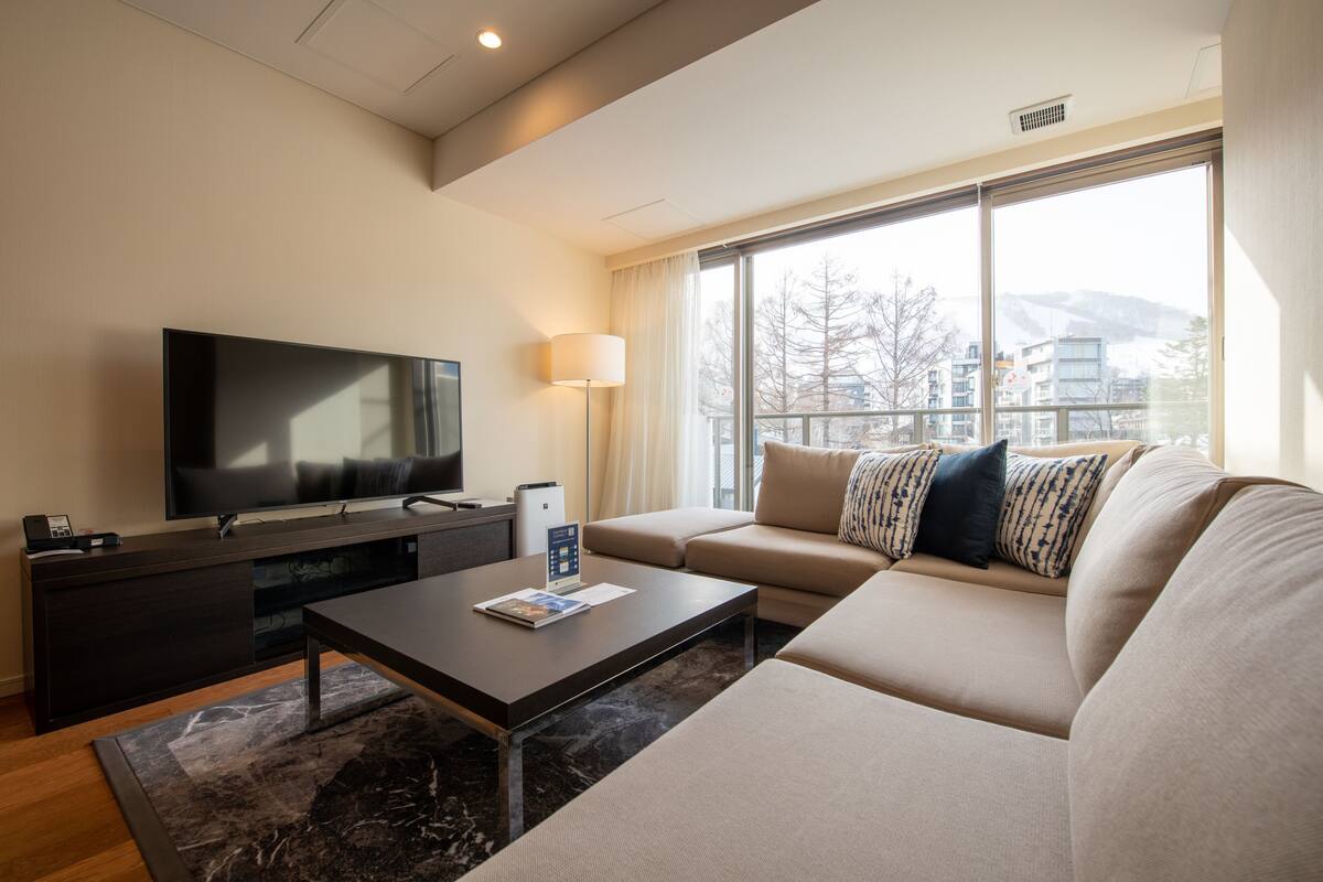 Una sala de estar moderna con un televisor de pantalla plana, un sofá, una mesa de centro y un ventanal con vistas a la ciudad.