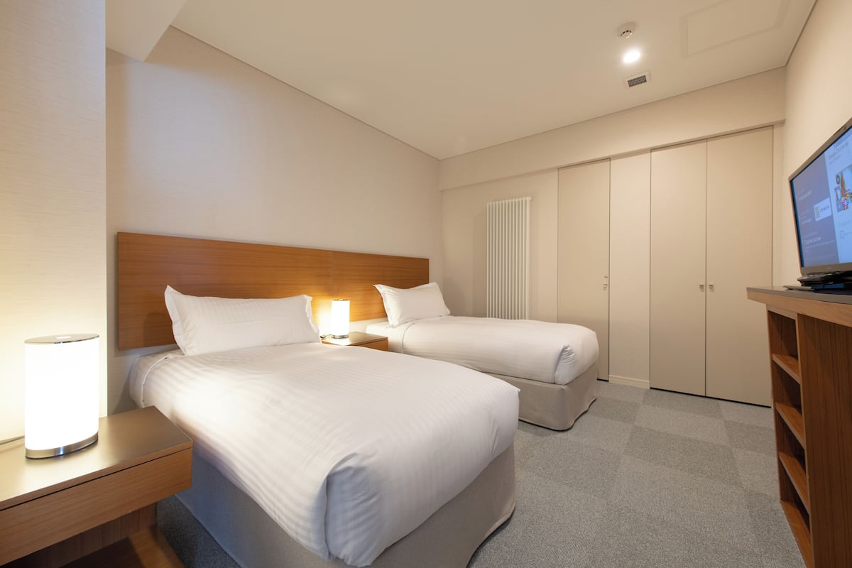 Habitación de hotel con dos camas, televisión, lámpara y armario.