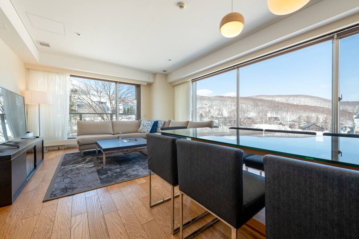 Una sala de estar moderna con una mesa de comedor de vidrio, sillas grises, un sofá y un televisor.