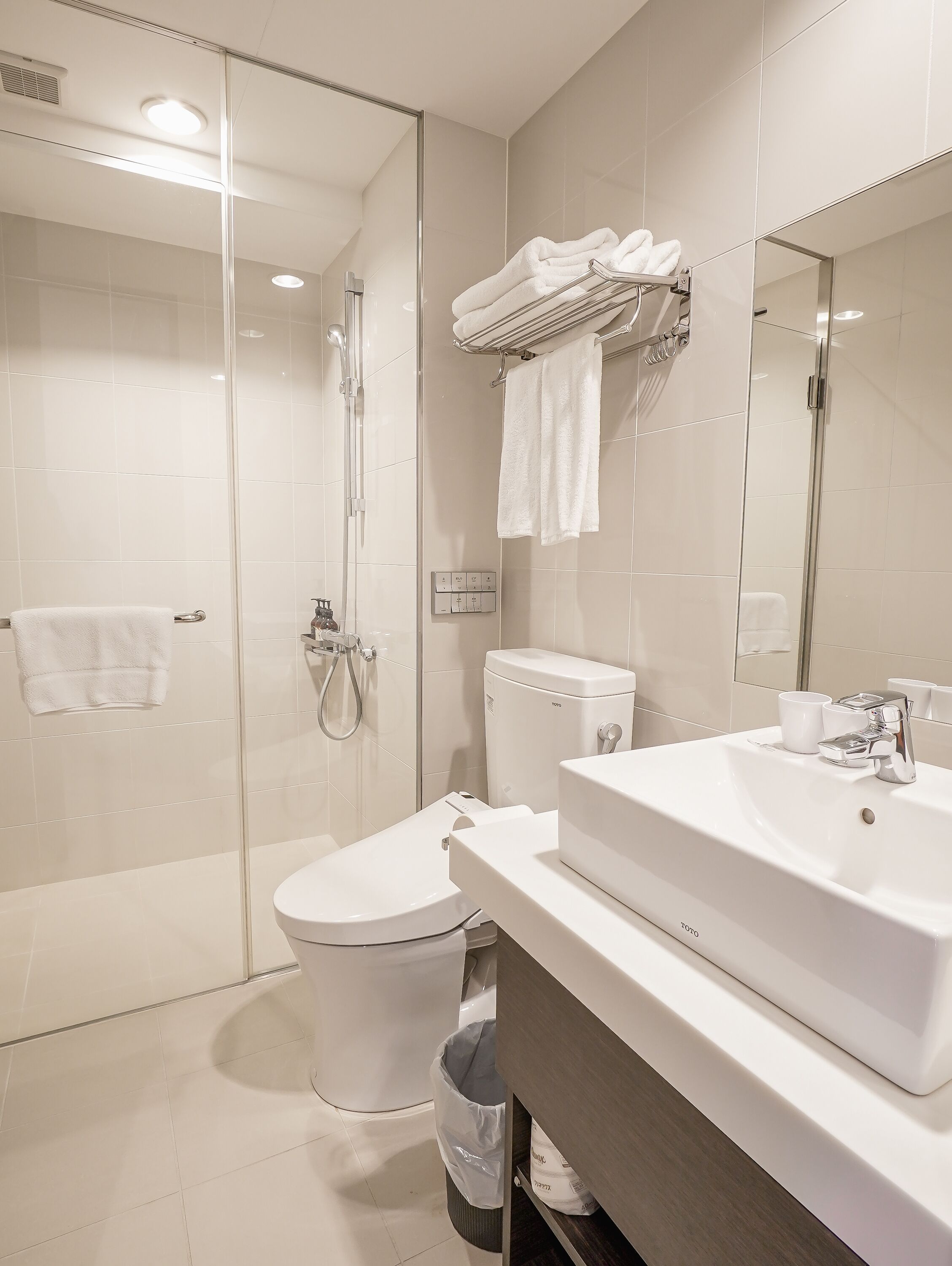 Ein modernes Badezimmer mit Duschkabine aus Glas, Toilette, Waschbecken und Handtuchhalter mit gefalteten Handtüchern.