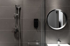 Un baño moderno con ducha, espejo redondo y lavamanos.