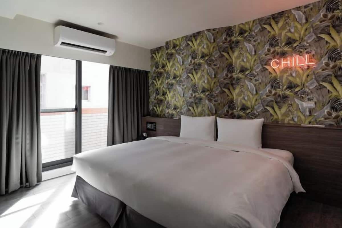 Una habitación de hotel con una cama grande, una mesita de noche, un letrero de neón y vistas al exterior.