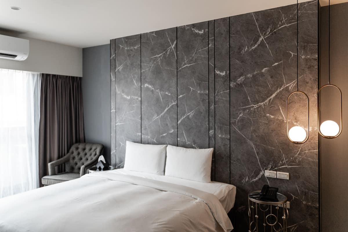 Una habitación de hotel moderna con una cama grande, una silla, una pared de mármol y una mesita de noche con teléfono.