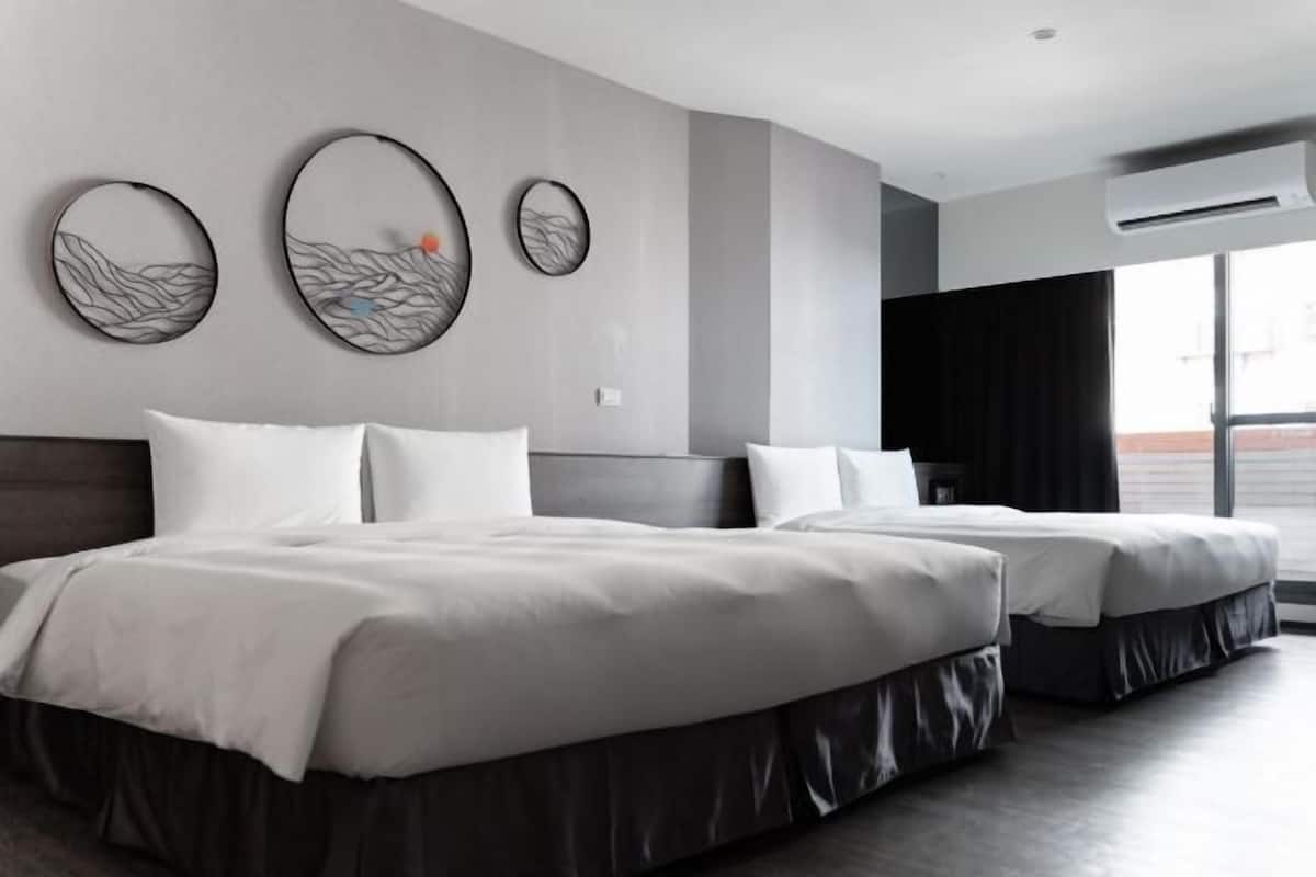 Habitación de hotel con dos camas, un ventanal grande y decoración en las paredes.