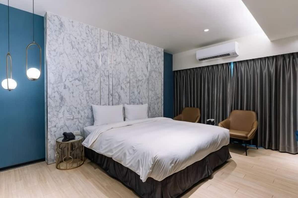 Una habitación de hotel moderna con una cama grande, dos sillas, una mesita redonda y una pared con diseño de mármol.