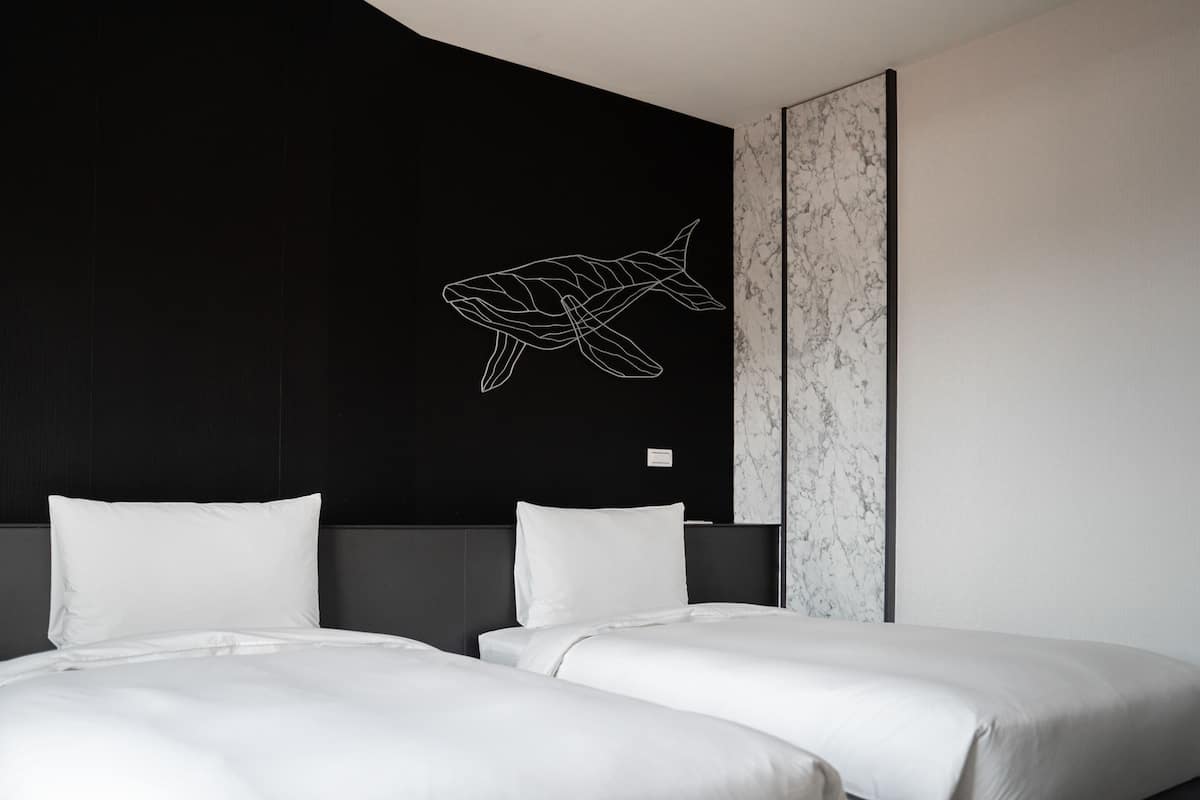 Habitación de hotel con dos camas, una pared negra con un dibujo de pez en blanco y un panel de mármol.
