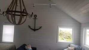 Et værelse med træpaneler, en lysekrone, en ankerdekoration og to vinduer med udsigt til grøn vegetation.