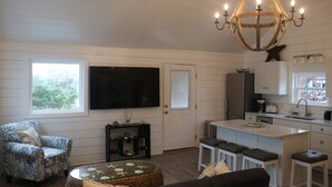 En rummelig stue med et stort fjernsyn, en behagelig lænestol og et spiseområde med bar.