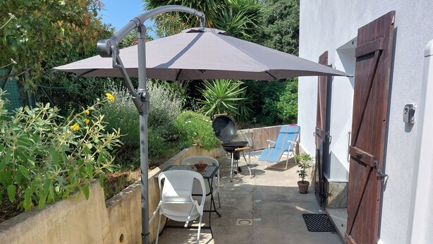 A patio with a table and chairs, a grill, and a wooden door.