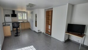 A modern kitchen with a microwave, refrigerator, and a dining area with a chair. There's a TV on a stand and a wooden cabinet.