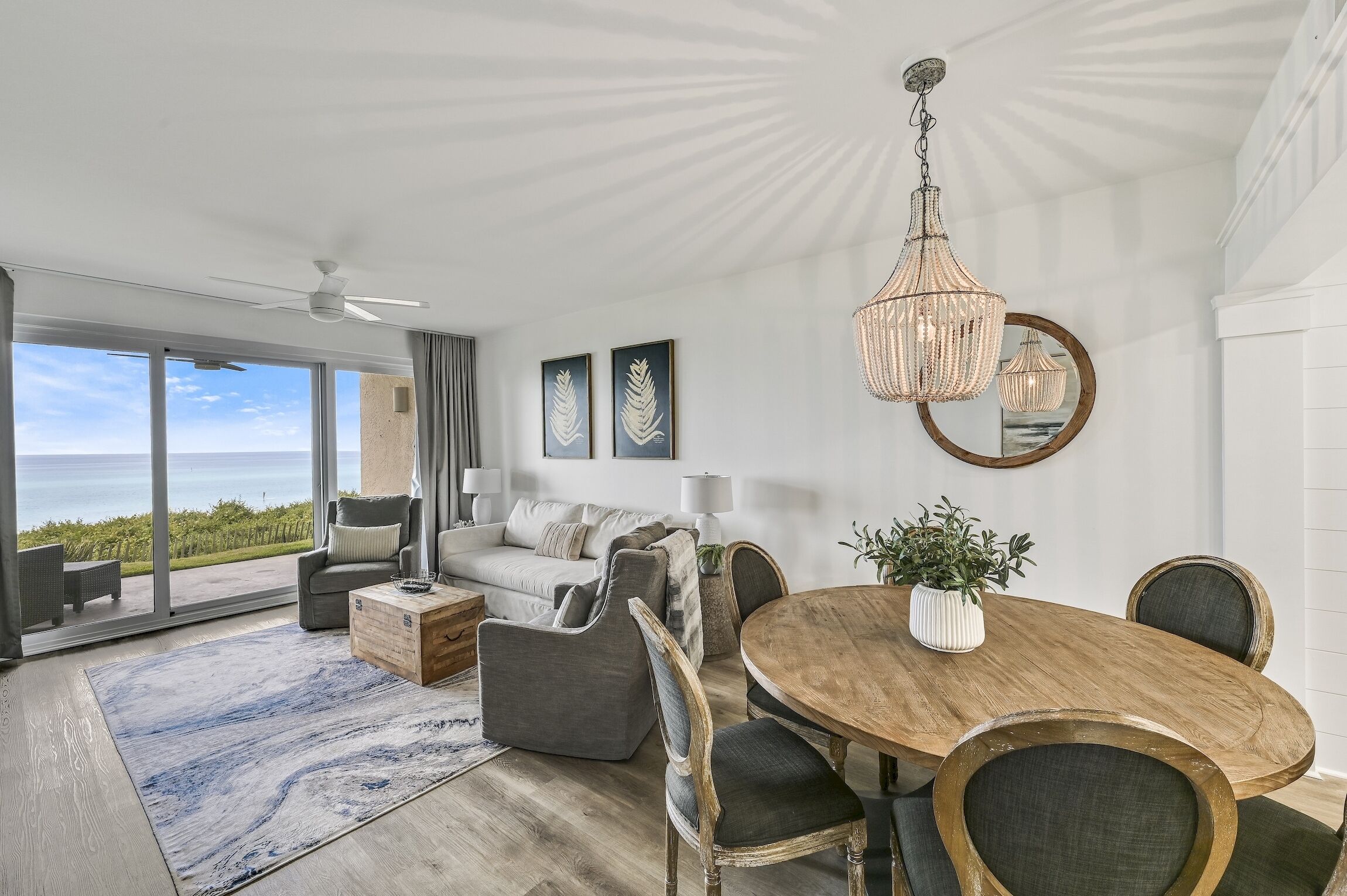 A modern living room with a large wooden dining table, comfortable seating, and a view of the ocean.