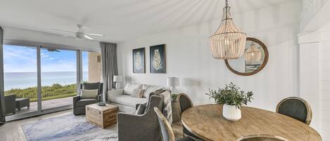 A modern living room with a large wooden dining table, comfortable seating, and a view of the ocean.