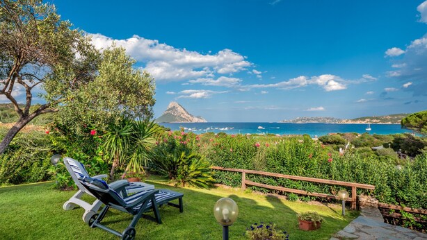 Ein Garten mit Rasen, einer Holzterrasse und Blick auf das Meer.