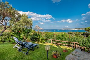 A garden with a lawn, a wooden deck, and a view of the sea. - Cottage Porto Taverna, 80 m from the Beach with Private Terrace & Garden (Loiri Porto San Paolo)