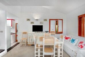 Un espacio habitable compacto con comedor, sofá, televisión y zona de cocina.