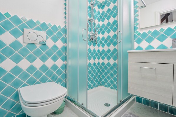 A bathroom with a glass-enclosed shower, a white toilet, and a tiled wall with a diamond pattern.