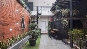 A courtyard with a brick wall, potted plants, a staircase, and outdoor seating. - URVANA Hotel By Majestra Hospitality (Bogor)