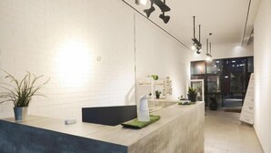 A reception area with a modern design, featuring a reception desk, potted plants, and a glass door leading to the outside. - URVANA Hotel By Majestra Hospitality (Bogor)