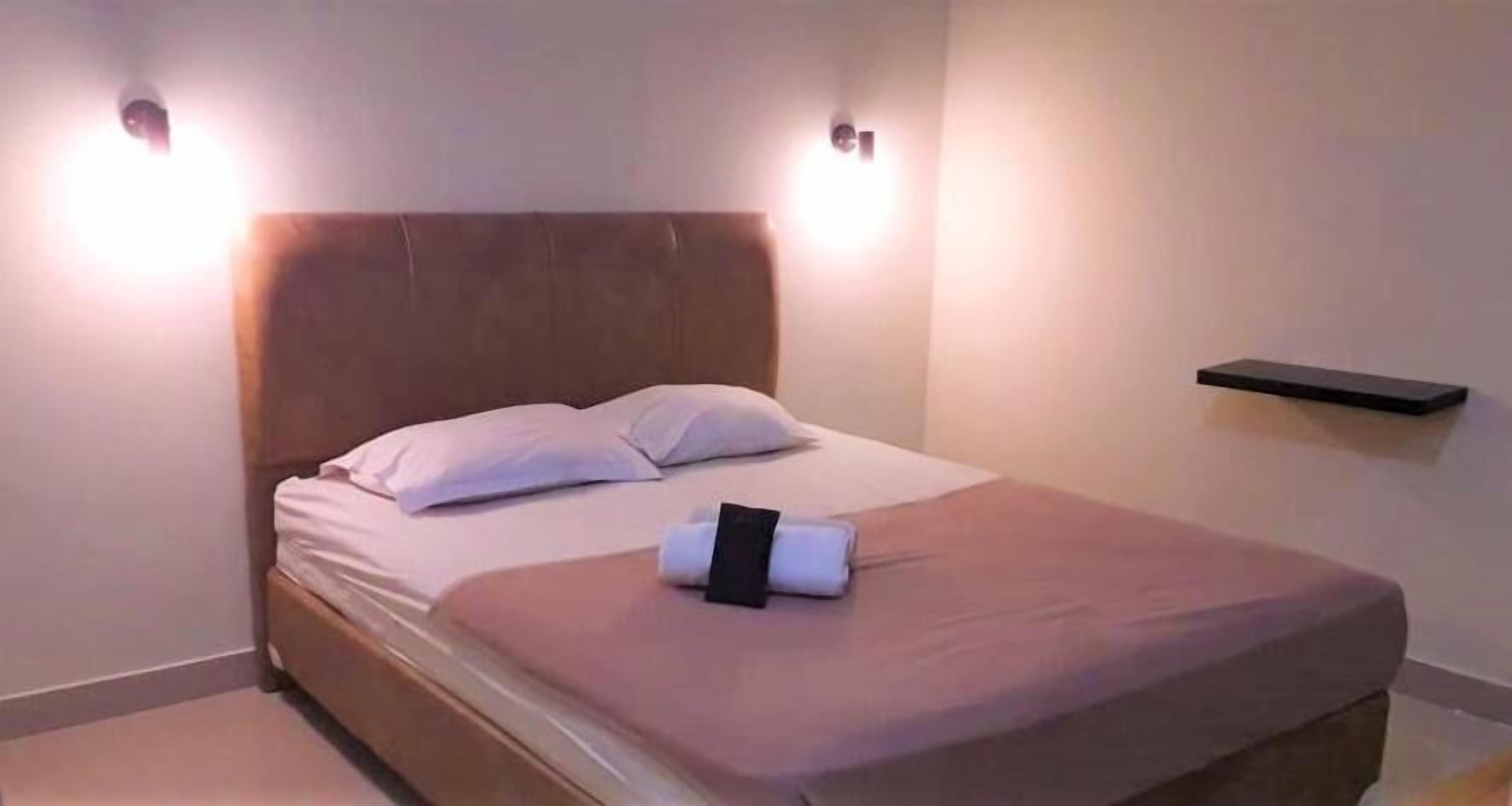 A neatly made bed with a headboard, a bedside table, and a wall-mounted shelf.