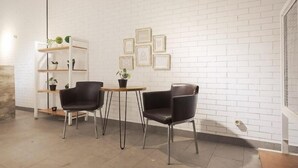 A modern room with white brick walls, two black leather chairs, a small round table, and a white shelving unit with potted plants. - URVANA Hotel By Majestra Hospitality (Bogor)