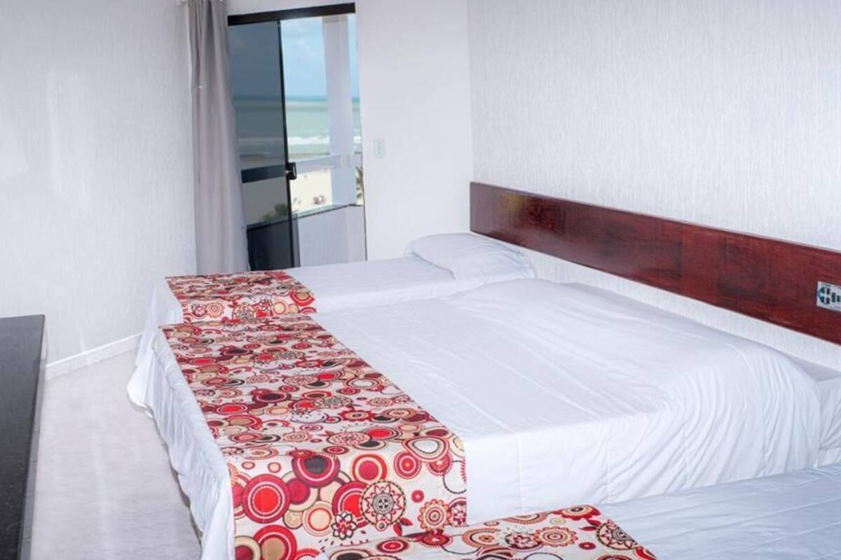 Habitación de hotel con una cama grande, televisor y vista al océano a través de una puerta corrediza.