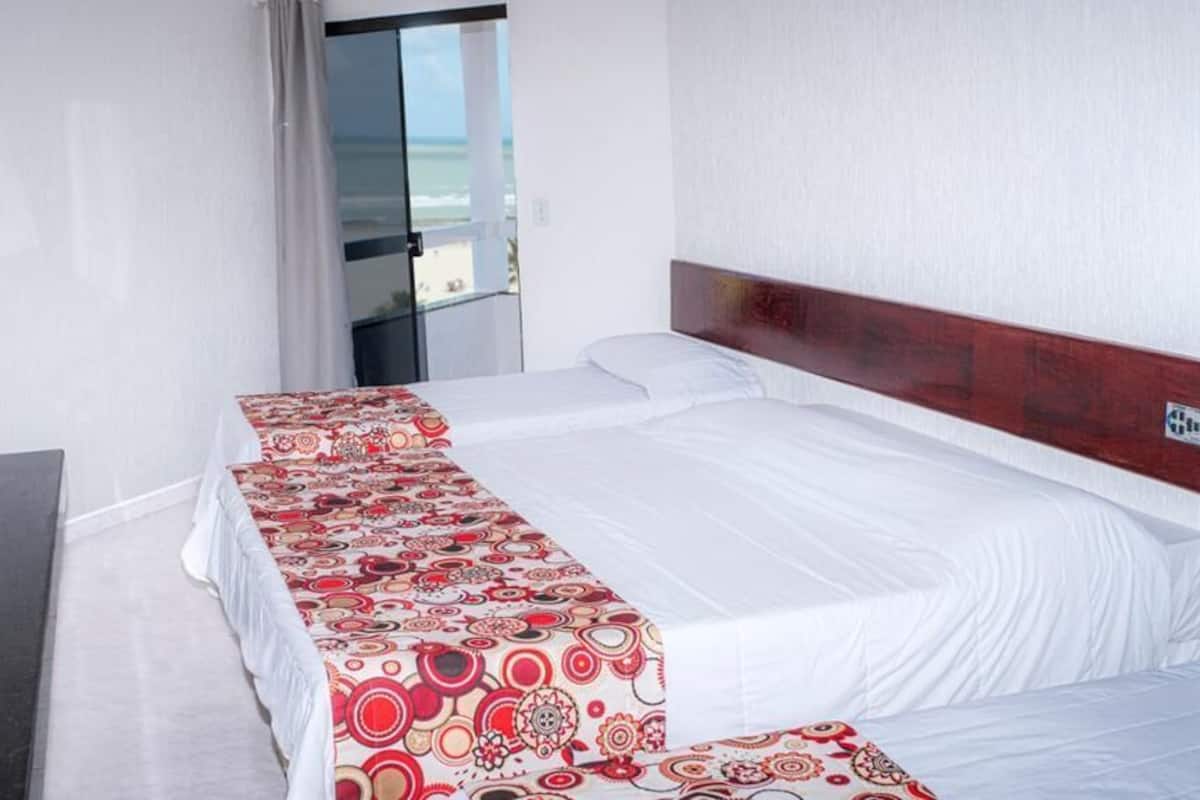 A hotel room with a large bed, a TV, and a view of the ocean through a sliding door.