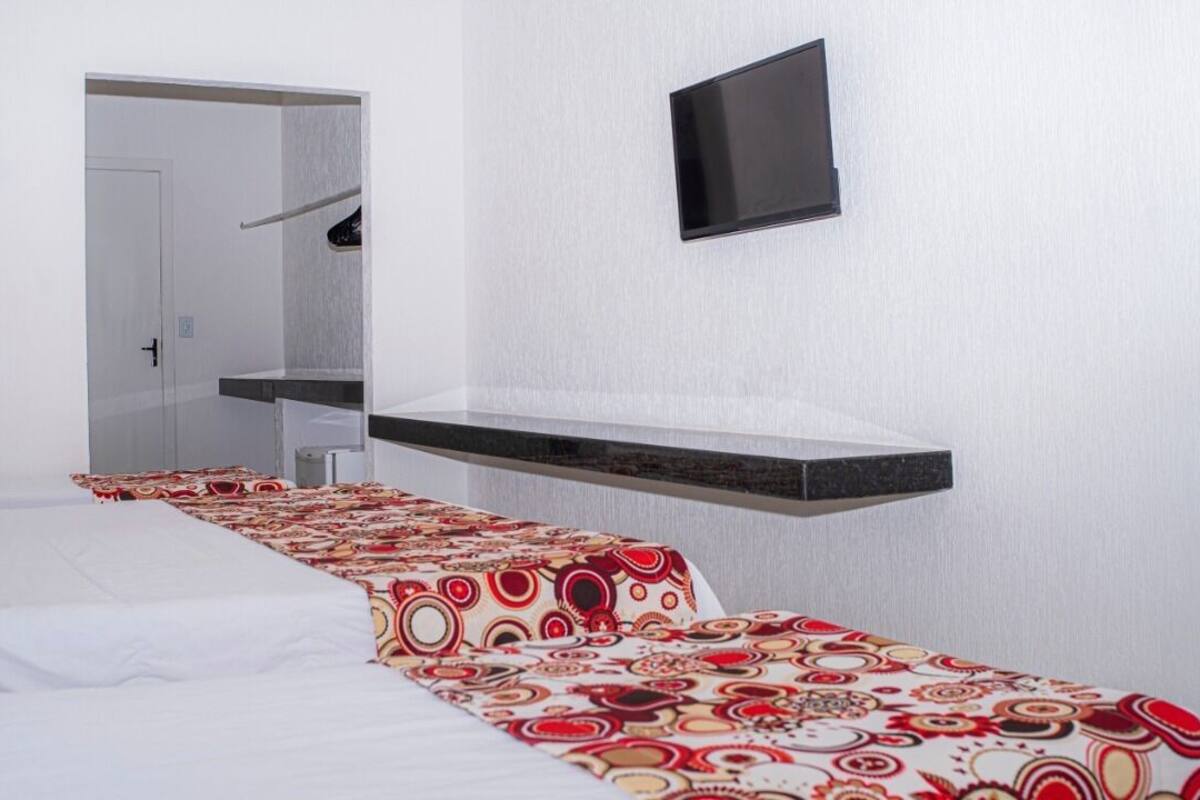 Una habitación de hotel con una cama, un televisor montado en la pared y un pequeño estante.