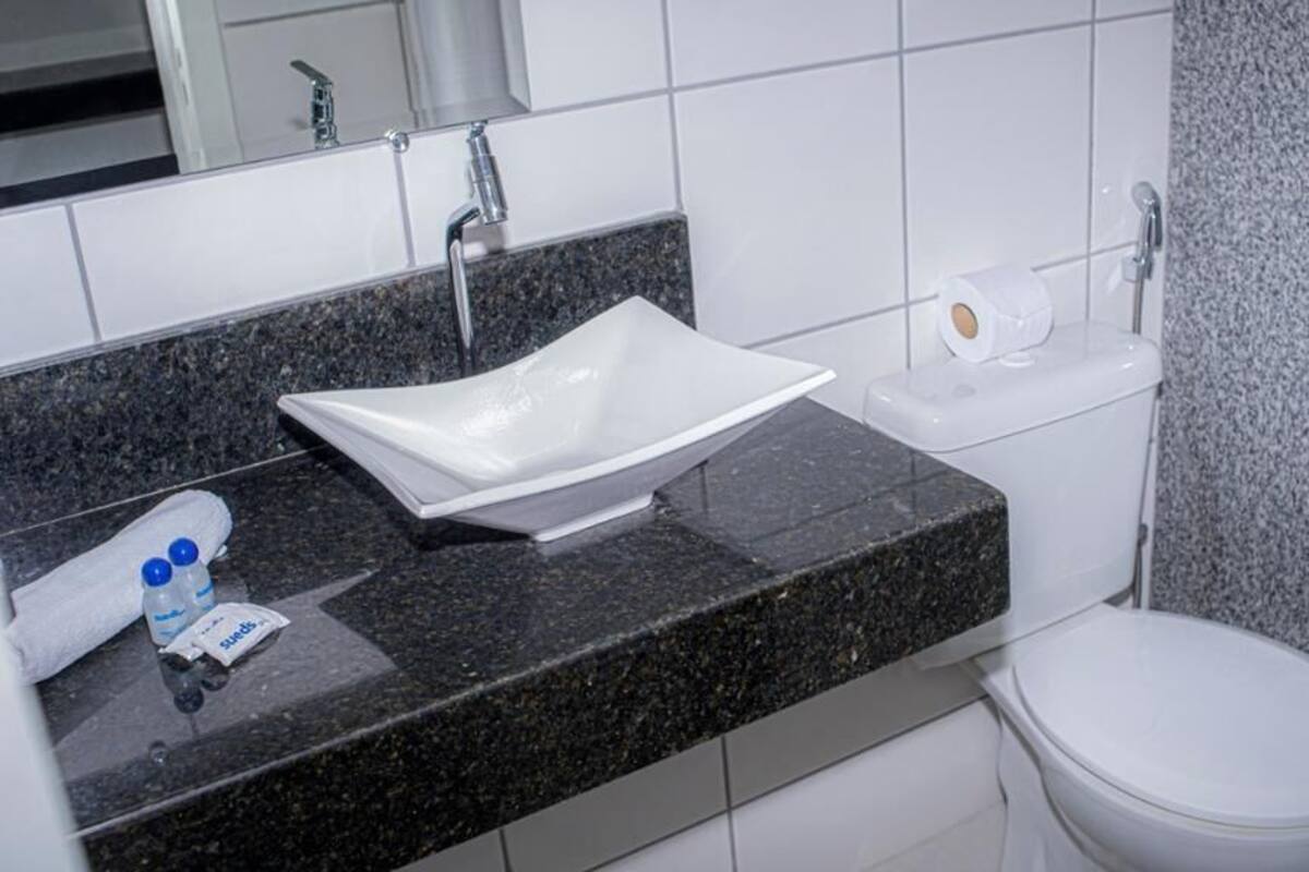 Un baño con lavamanos blanco, espejo, inodoro y toallero.