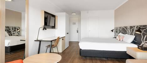A hotel room with a bed, a desk, a chair, and a TV.