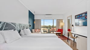 Habitación de hotel con dos camas, un escritorio, una silla, un televisor y un balcón con mesa y sillas.