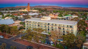 Un hotel de varios pisos con techo plano, rodeado de árboles y automóviles estacionados.