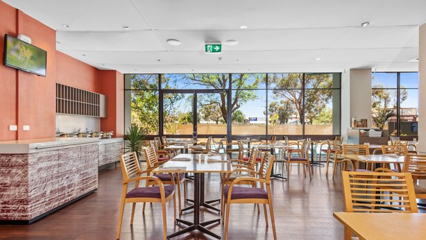 Un restaurante espacioso con mesas y sillas de madera, una zona de cocina y amplios ventanales que ofrecen vistas al exterior.