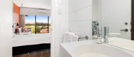 Un baño moderno con un lavabo blanco grande, un espejo y vistas a un paisaje urbano a través de una ventana.