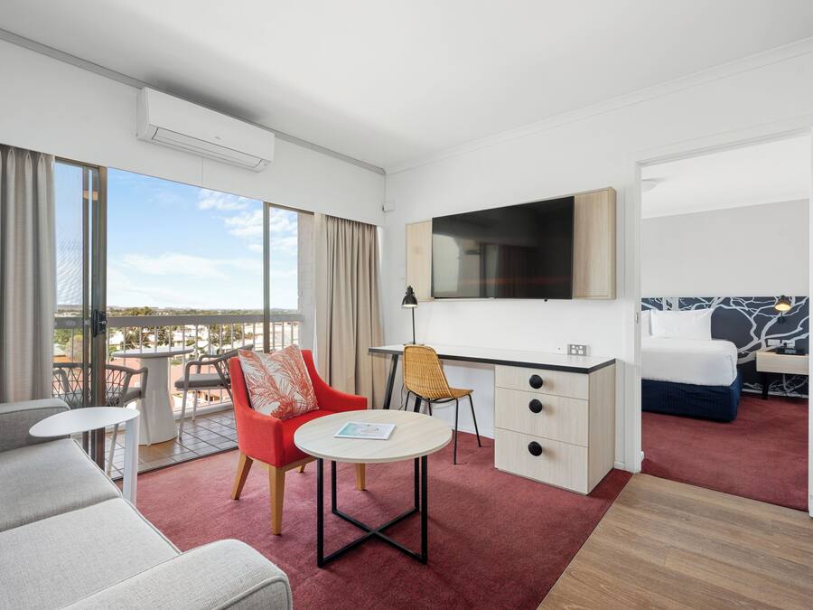 A modern hotel room with a balcony, a flat-screen TV, a desk, a sofa, and a bed.