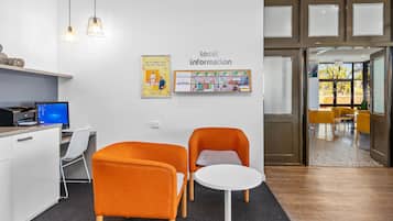 Et moderne kontor med to orange stole, et hvidt bord, en computer og et skilt med 'lokal information' på væggen.