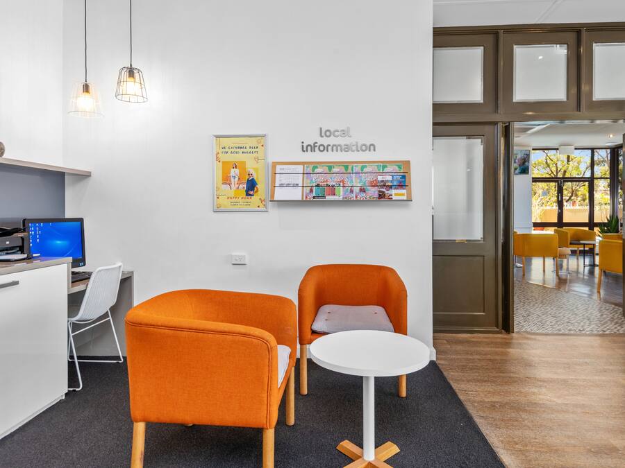 Et moderne kontor med to orange stole, et hvidt bord, en computer og et skilt med 'lokal information' på væggen.