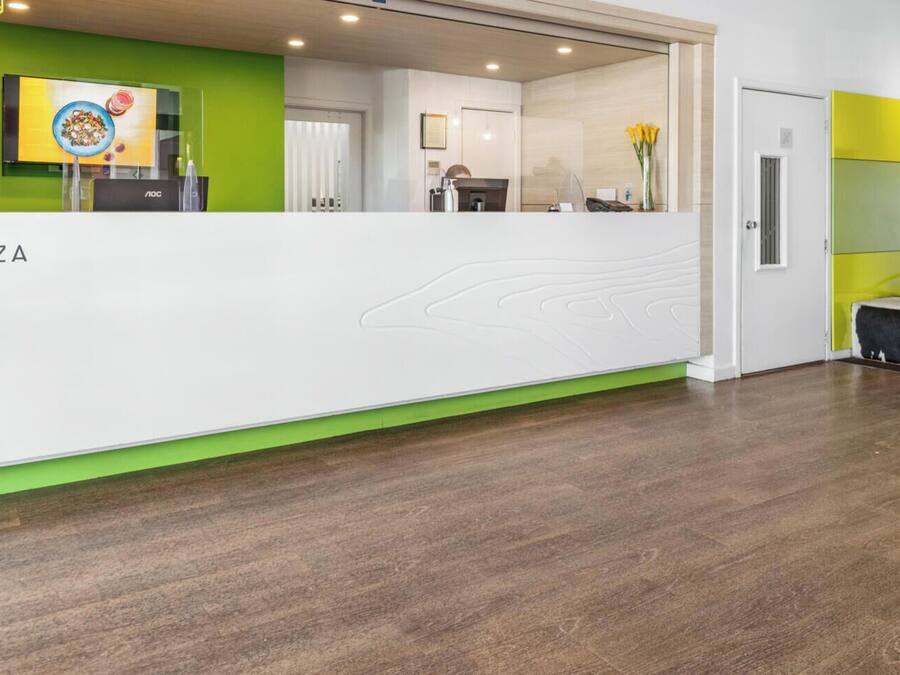 A hotel reception desk with a green accent wall, a framed picture, and a reception area leading to a seating area with a unique black and white design.