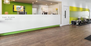 Ein Hotelrezeptionstresen mit grüner Akzentwand, einem gerahmten Bild und einem Empfangsbereich, der in einen Sitzbereich mit einem markanten schwarz-weißen Design übergeht.